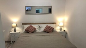 A neatly made bed with two pillows, two bedside lamps, a nightstand, and a mirror above the bed. - Rooms Radunica street (Split)