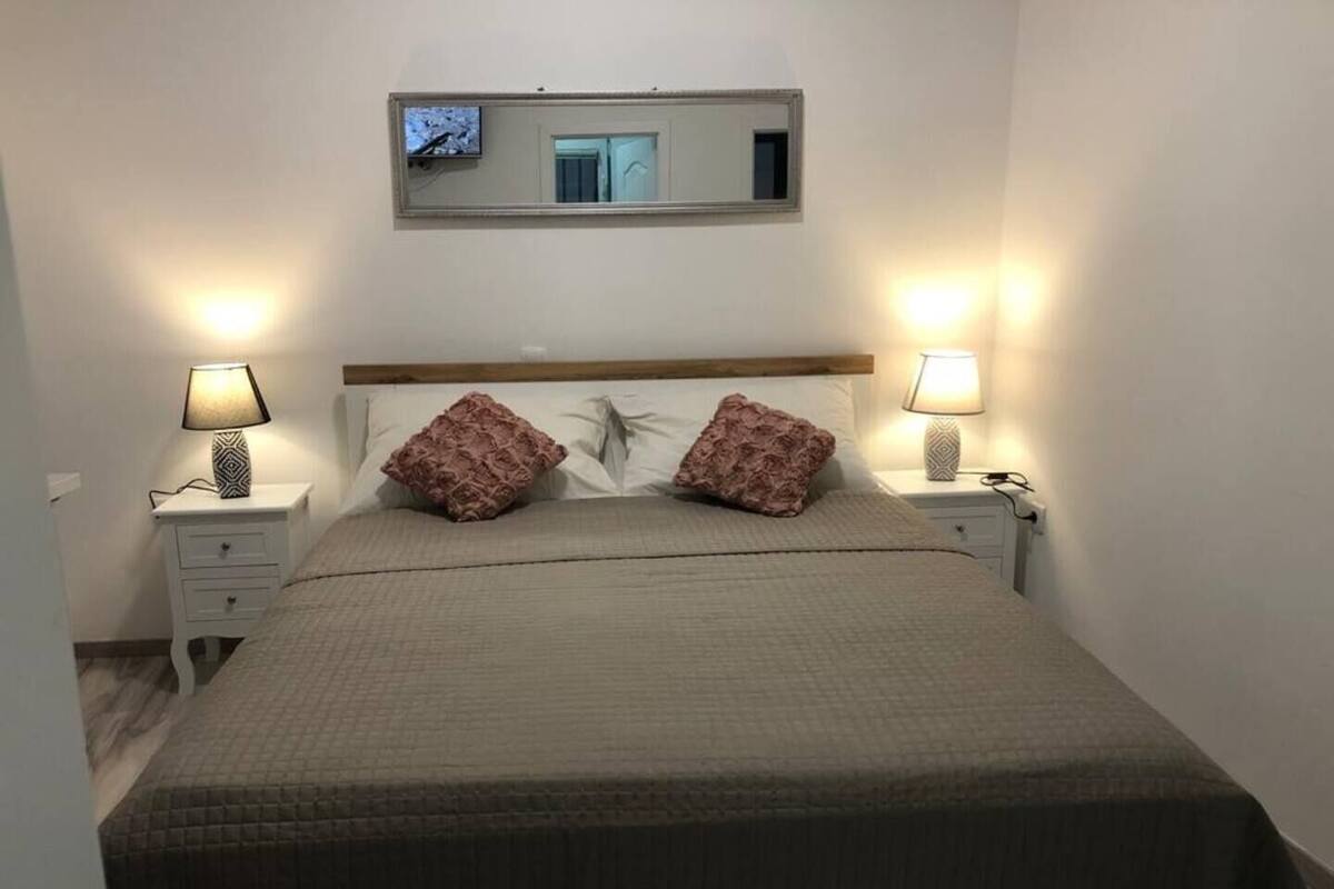 A neatly made bed with two pillows, two bedside lamps, a nightstand, and a mirror above the bed.