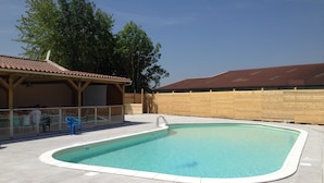 Una piscina con un borde de baldosas, una zona de estar techada y una valla de madera.