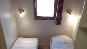 Habitación pequeña con dos camas individuales, una ventana con cortinas y luces fijadas a la pared.
