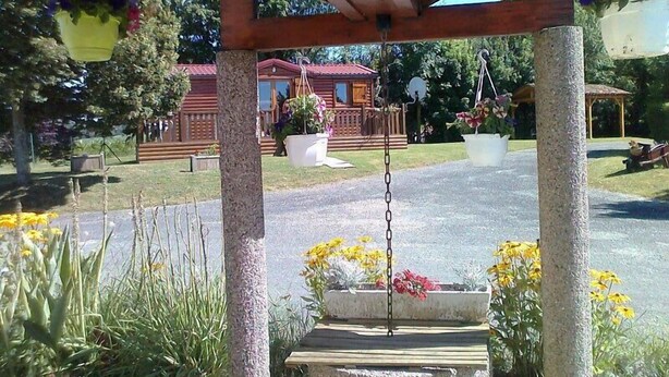 A wooden pergola with hanging flower pots and a swing. - Camping La Croix Badeau Tentes équipées (Soulaines-Dhuys)