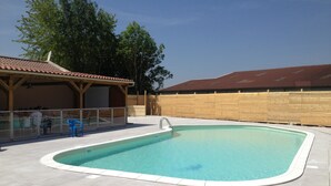 A swimming pool with a tiled deck, a covered seating area, and a wooden fence. - Camping La Croix Badeau Tentes équipées (Soulaines-Dhuys)