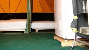 A tent with a bed, a white appliance, and a shelf with items. - Camping La Croix Badeau Tentes équipées (Soulaines-Dhuys)