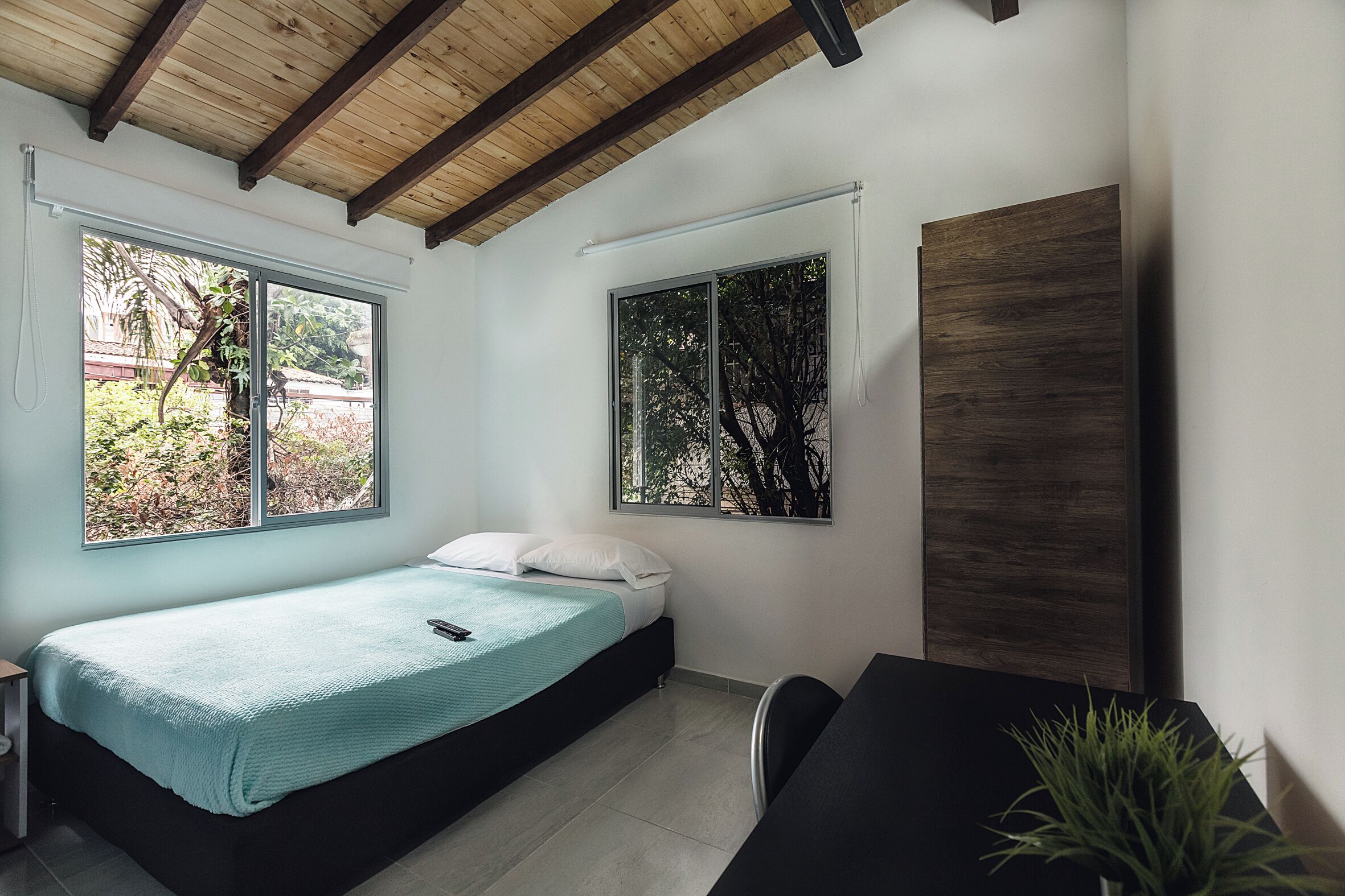 A modern bedroom with a bed, a desk, and a large window.