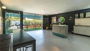 A modern kitchen with a central island, a dining area with a bench, and a view of the outdoor garden. - Living Hostal - Hostel (Medellín)