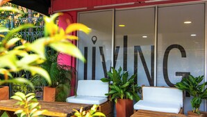An outdoor seating area with wooden tables and white cushioned chairs, surrounded by potted plants. - Living Hostal - Hostel (Medellín)