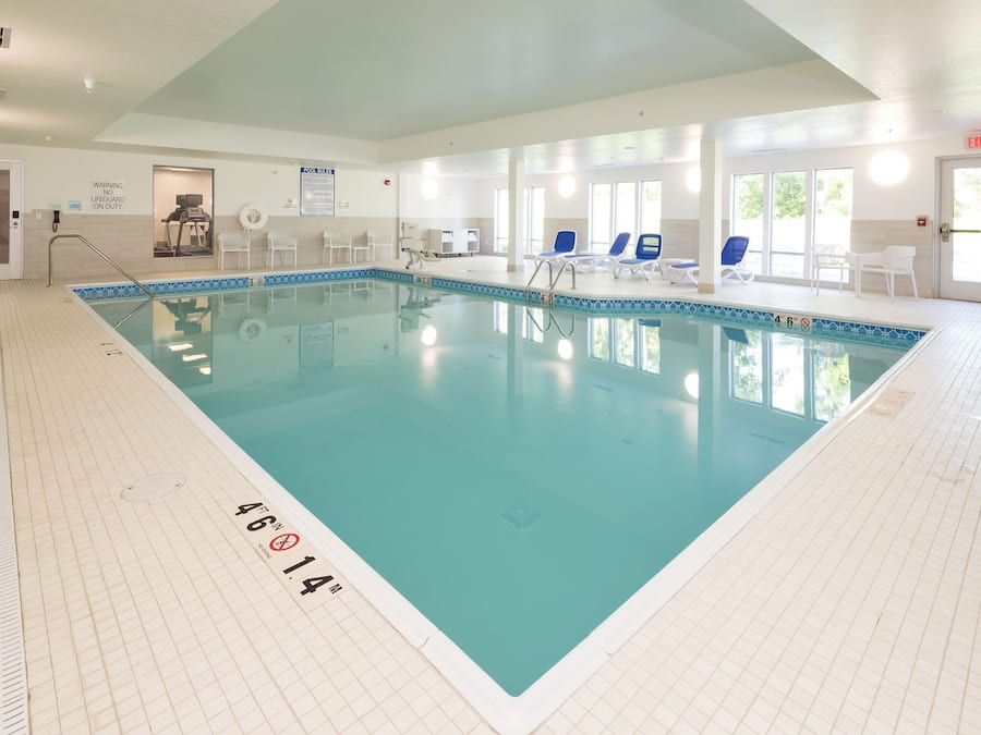 A large indoor swimming pool with clear water, surrounded by lounge chairs and a tiled floor.