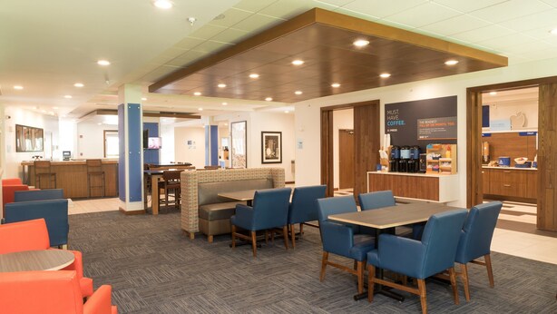 A modern hotel lobby with seating areas, a coffee station, and a reception desk.