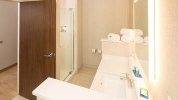 Un bagno moderno con una porta in legno, cabina doccia in vetro, lavabo bianco e specchio con porta asciugamani.