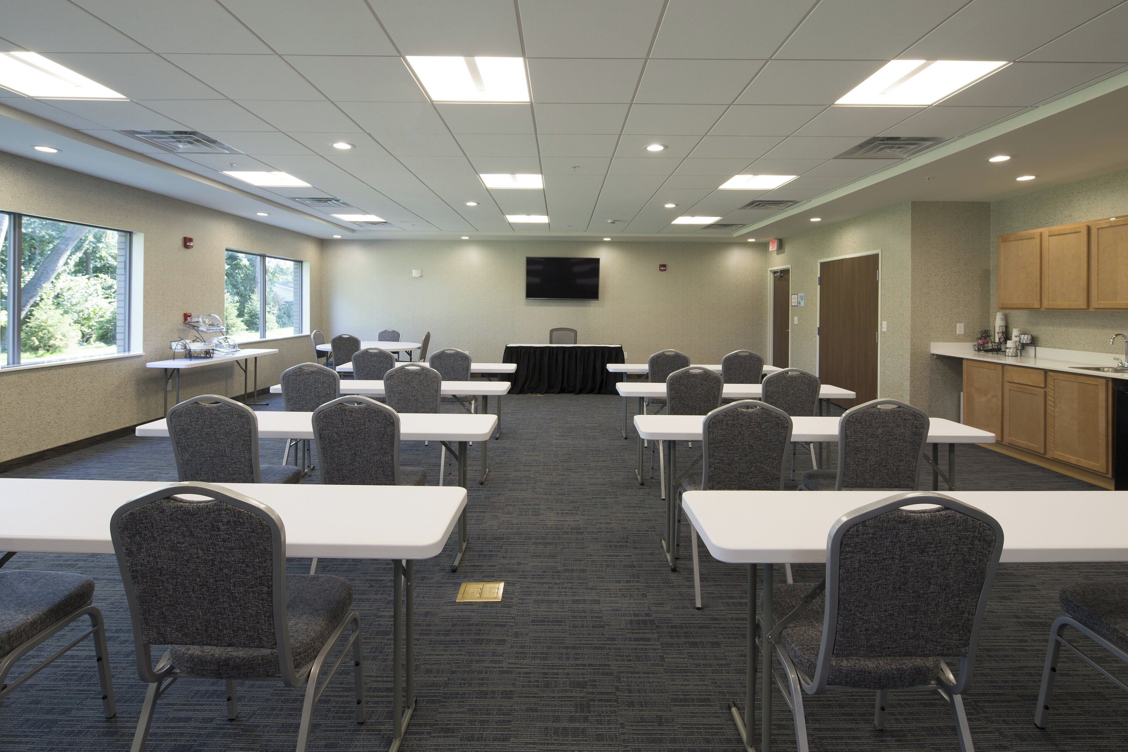 A conference room with tables and chairs, a large screen, and a kitchenette.