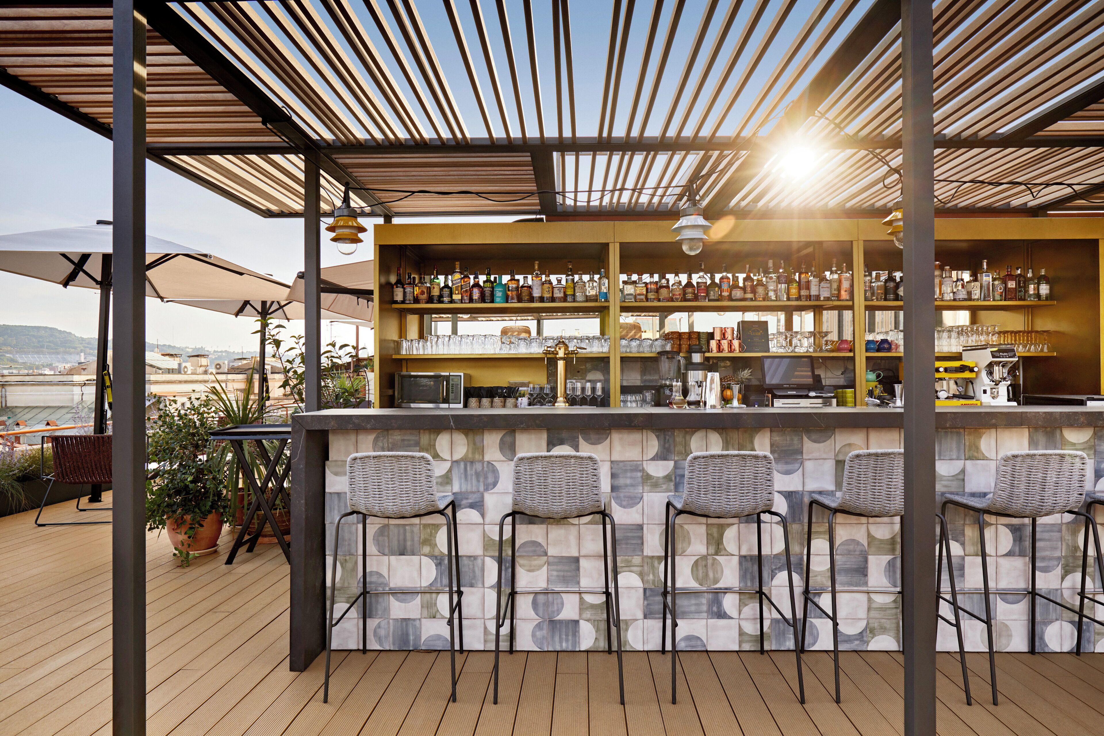 An outdoor bar area with a wooden deck, bar stools, and a variety of bottles and glasses on shelves.