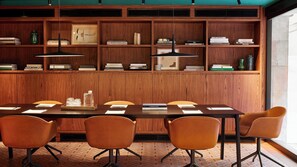 A conference room with a long table, six chairs, wooden paneling, and bookshelves with various books.