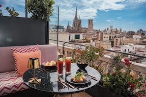 A balcony with a dining table, a sofa, and a view of a cityscape including a cathedral. - Kimpton Vividora Hotel by IHG (Barcelona)