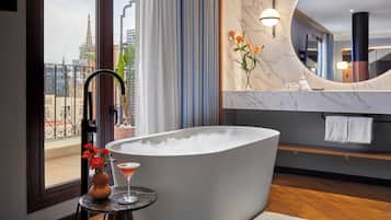 Un baño moderno con una bañera independiente, un espejo redondo y vistas de la ciudad a través de un ventanal grande.