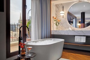 A modern bathroom with a freestanding bathtub, a round mirror, and a view of the cityscape through a large window. - Kimpton Vividora Hotel by IHG (Barcelona)