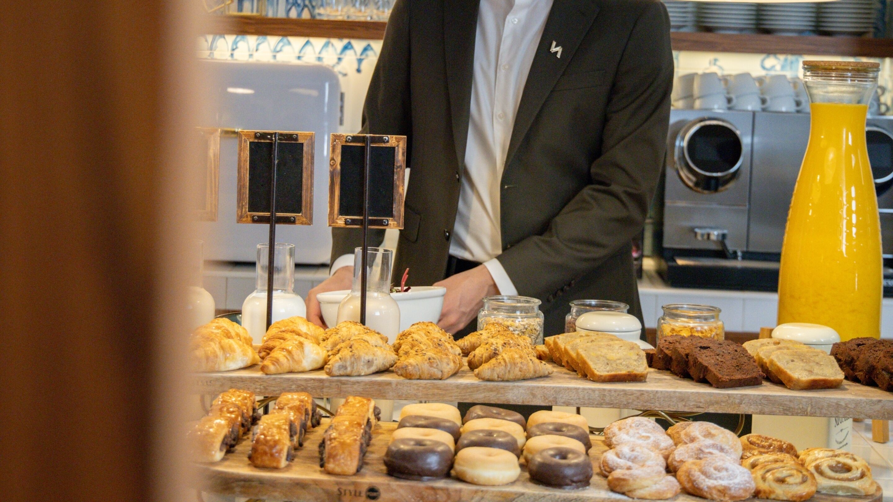 A bakery display with various baked goods and a person in a suit behind the counter.