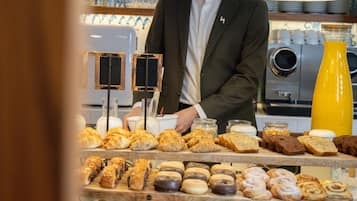 Mostrador de una panadería con diferentes productos horneados y una persona con traje detrás.