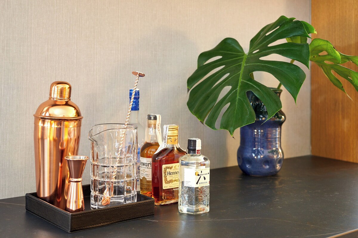 A bar setup with copper cocktail shakers, a glass carafe, and bottles of liquor on a tray.