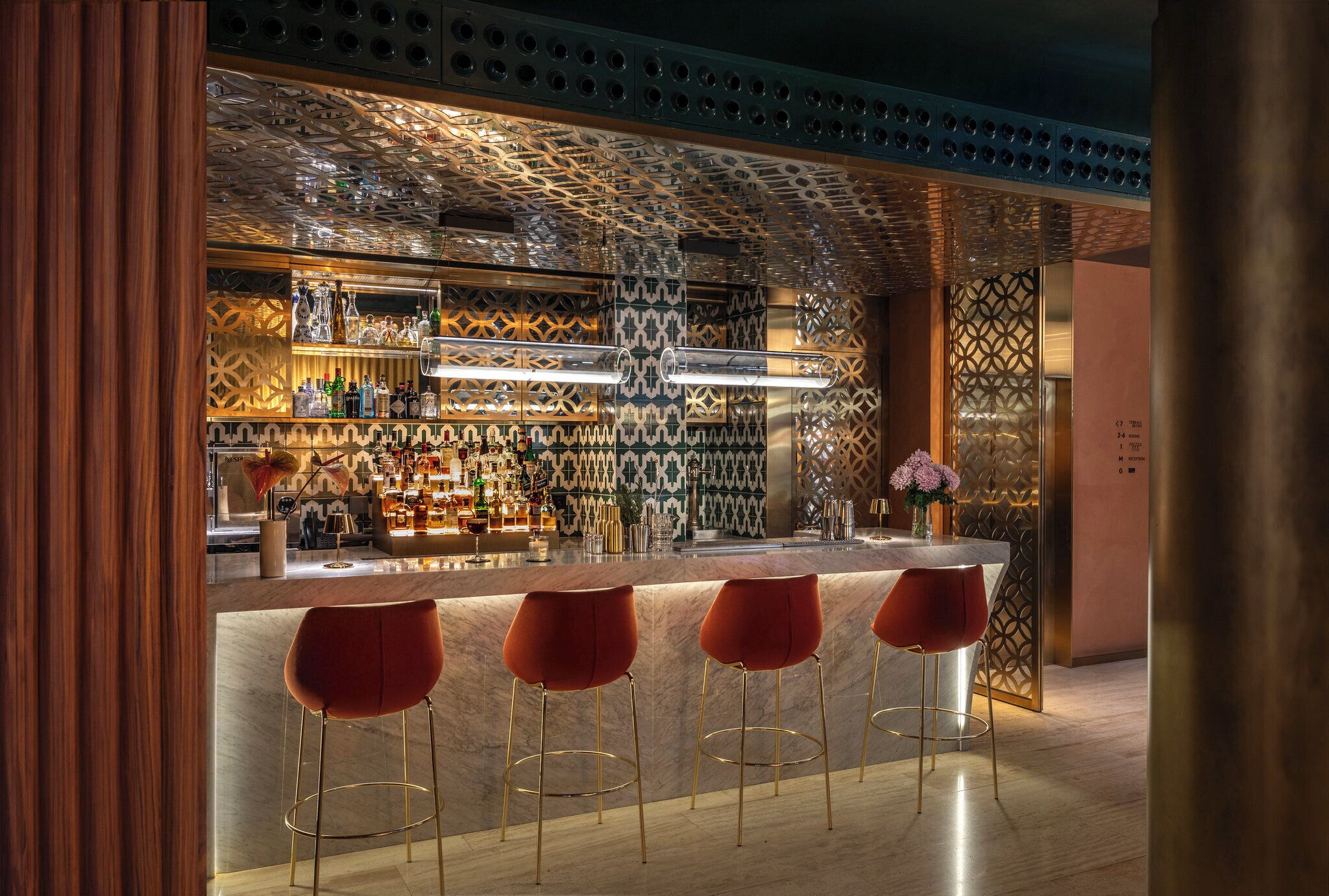 A bar area with a patterned ceiling, a marble countertop, and three red bar stools.