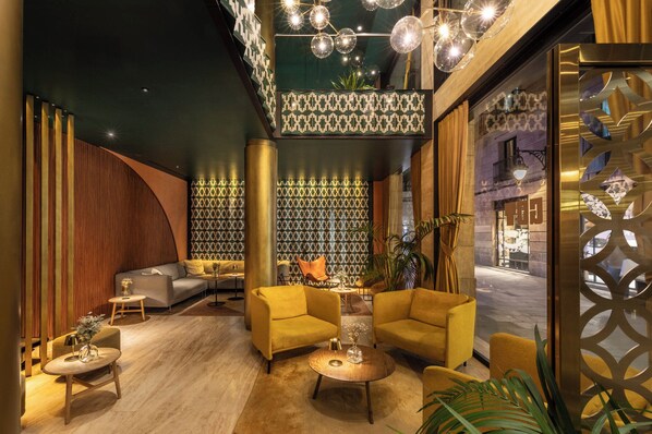 A lobby with a modern design, featuring a sofa, armchairs, and a coffee table. There is a patterned wall and a decorative ceiling light fixture. - Kimpton Vividora Hotel by IHG (Barcelona)