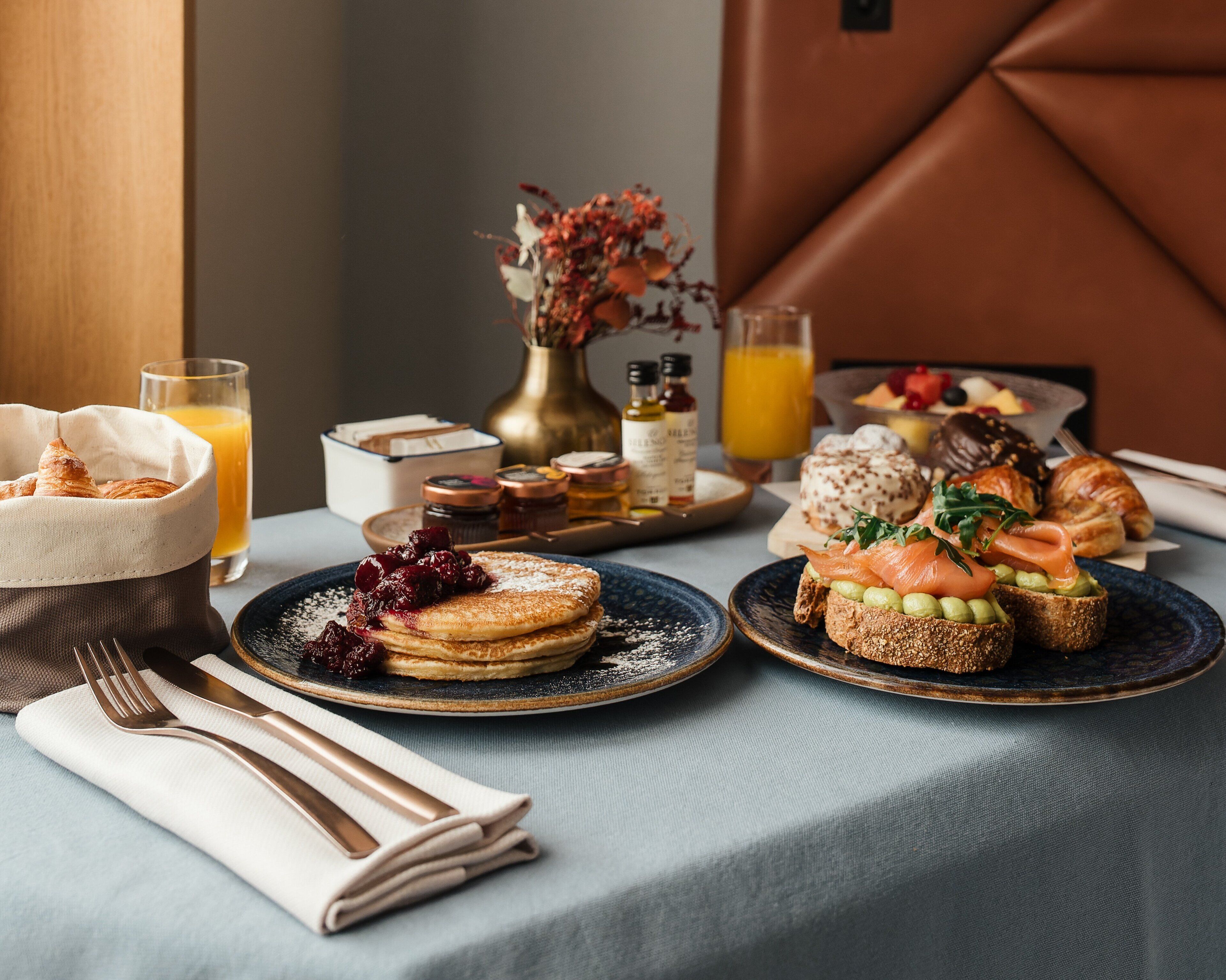 Ein Frühstücksbuffet mit Gebäck, Sandwiches und einer Obstschale auf einem Tisch.