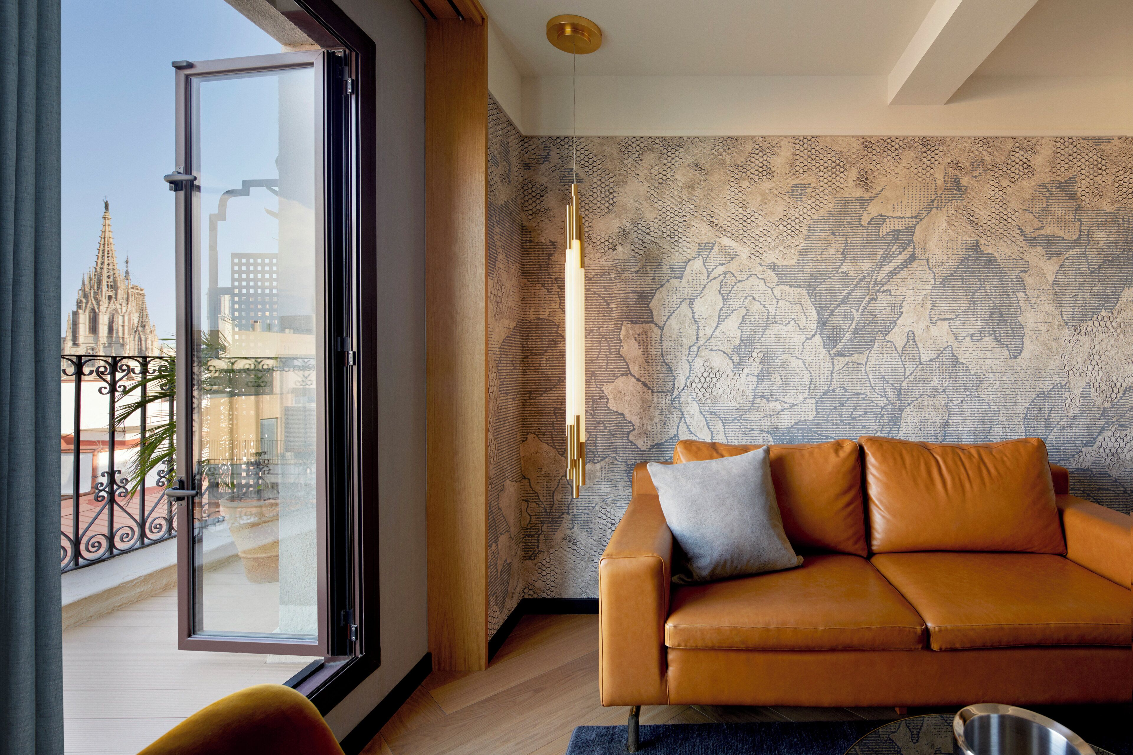 A modern living room with a leather sofa, a patterned wallpaper, and a view of a cathedral through a glass door.