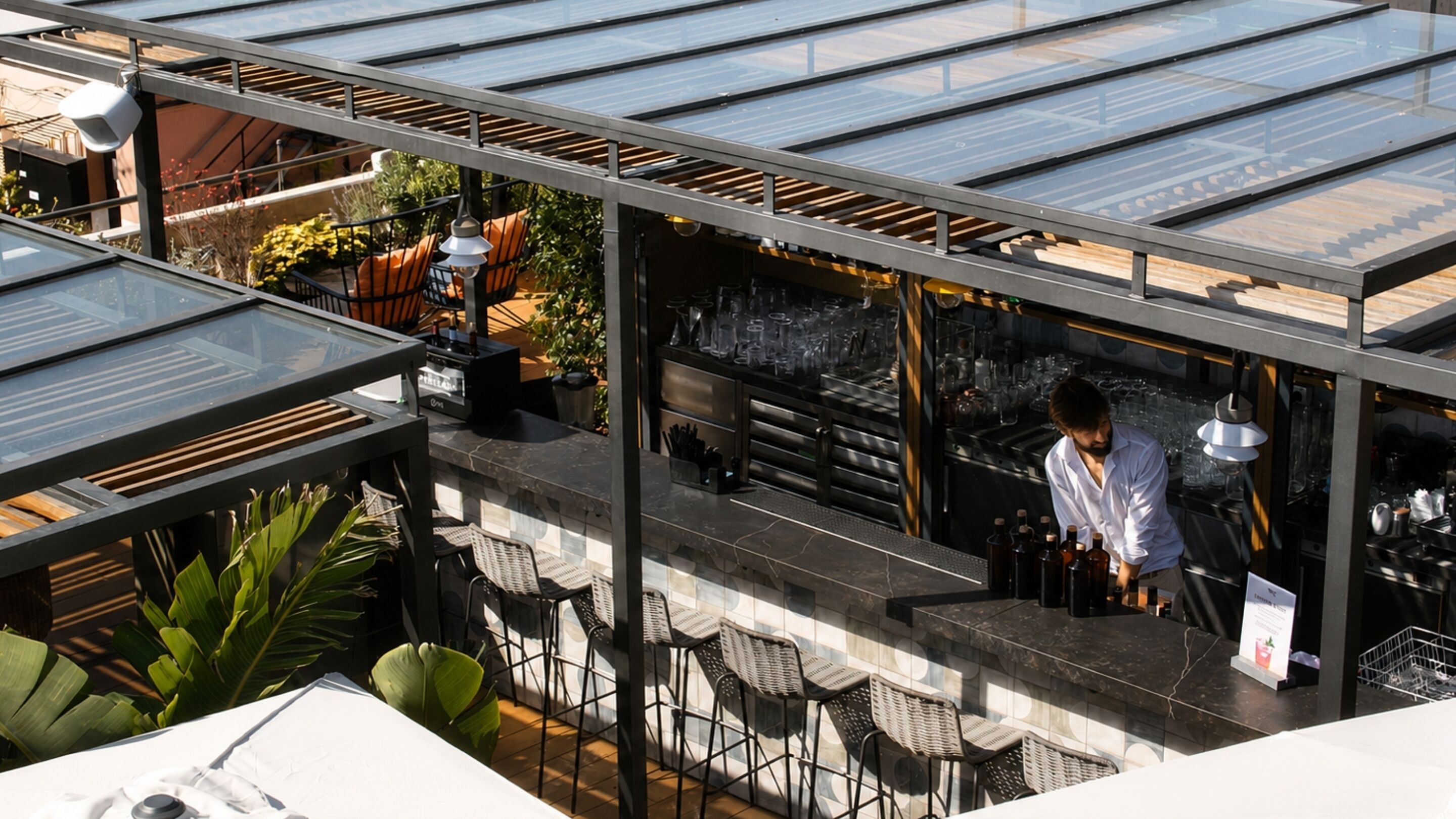 A rooftop bar with a glass ceiling, outdoor seating, and a bartender.