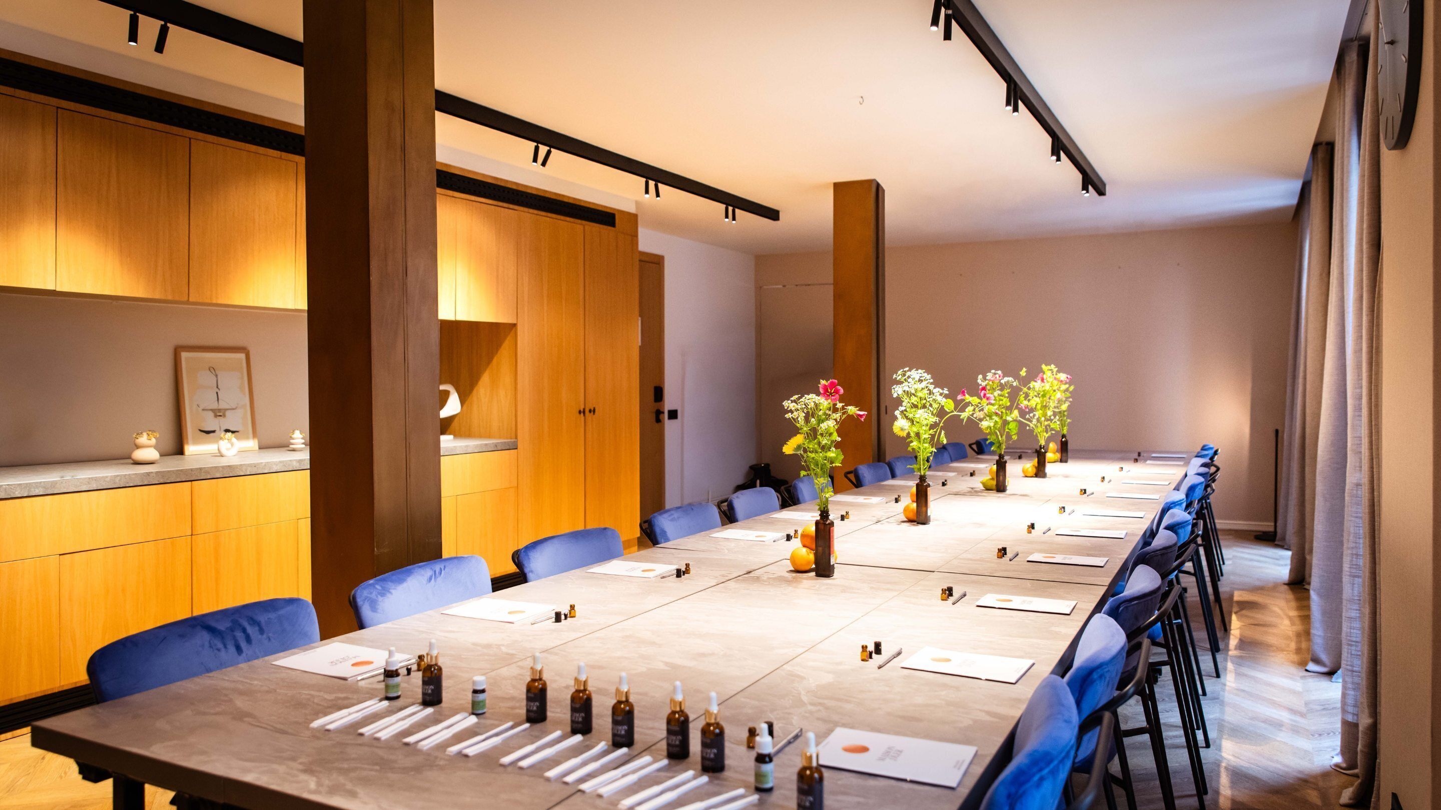 A conference room with a long table, blue chairs, and vases with flowers.
