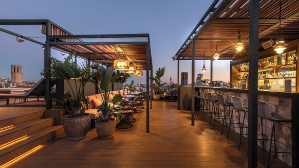 An outdoor bar area with wooden flooring, potted plants, and seating arrangements. - Kimpton Vividora Hotel by IHG (Barcelona)