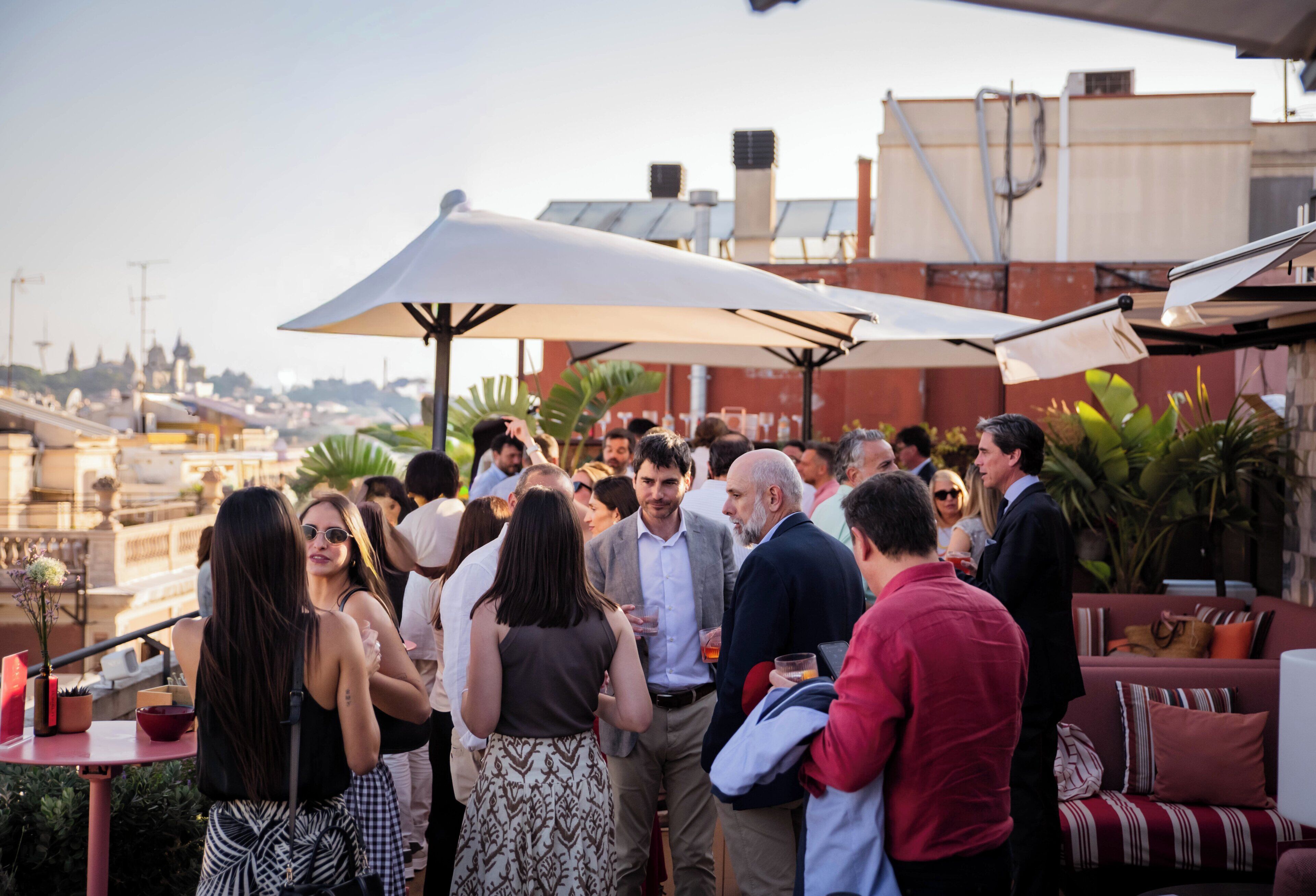 Un encuentro en la azotea con gente conversando, mobiliario exterior y un paisaje urbano de fondo.