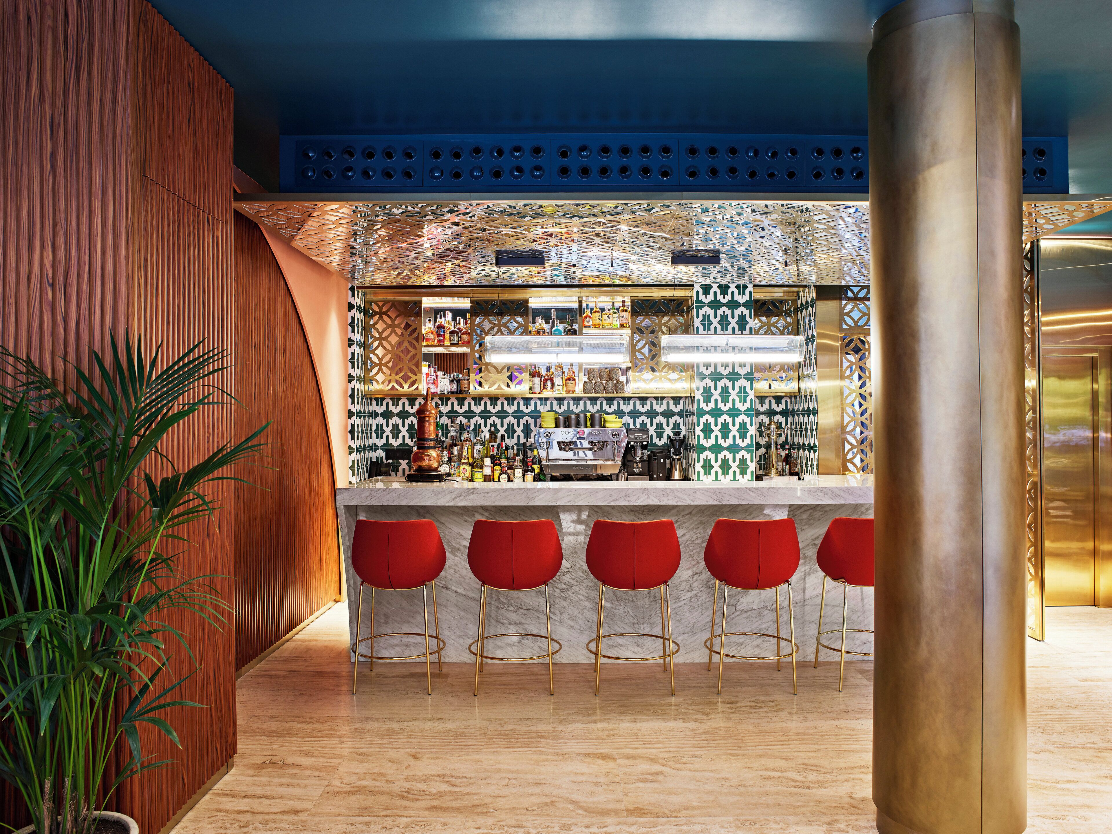 A bar area with a patterned wall, a counter with various bottles, and four red bar stools.