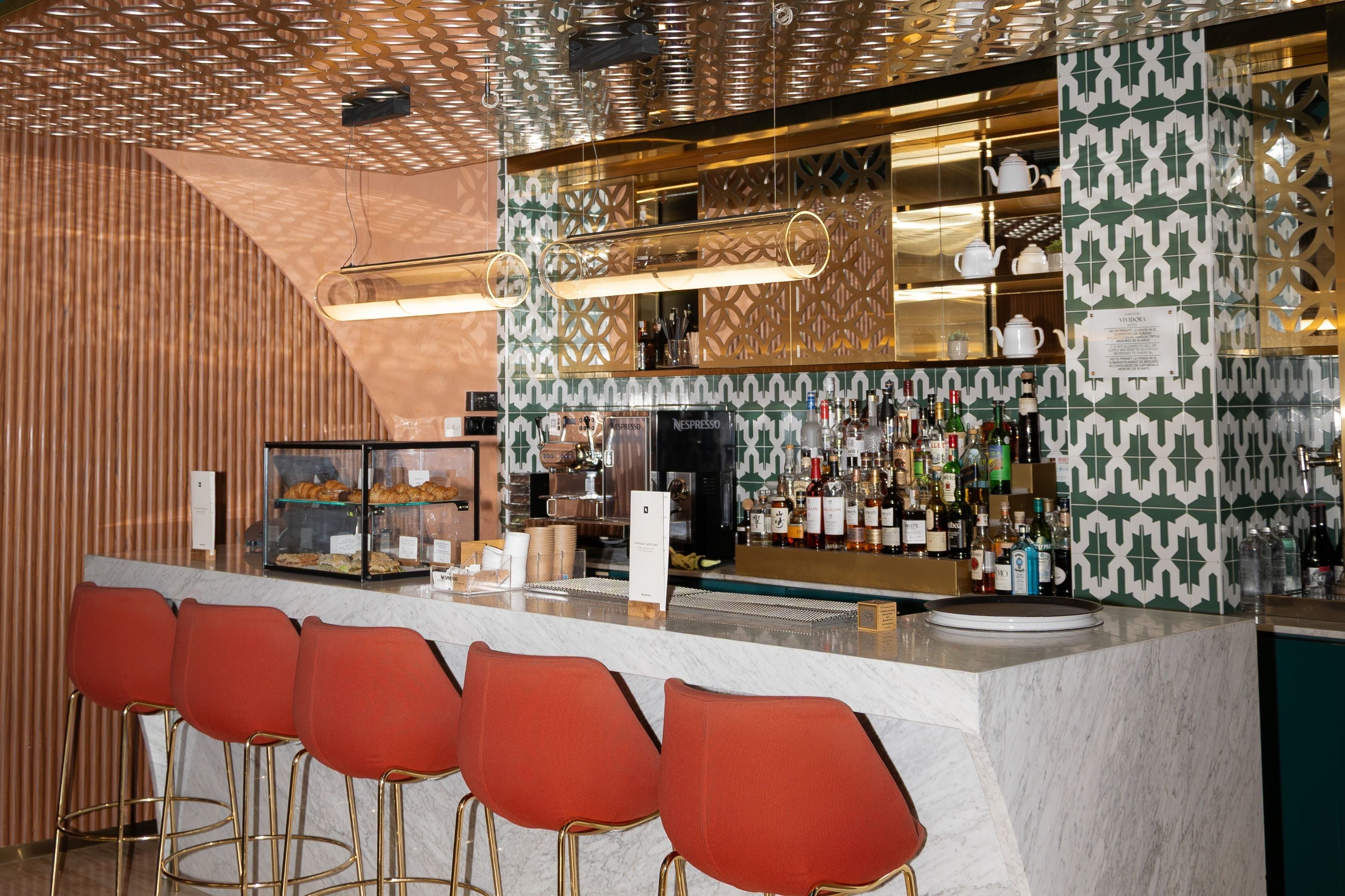 Una zona de bar con mostrador, taburetes y una vitrina con pasteles.