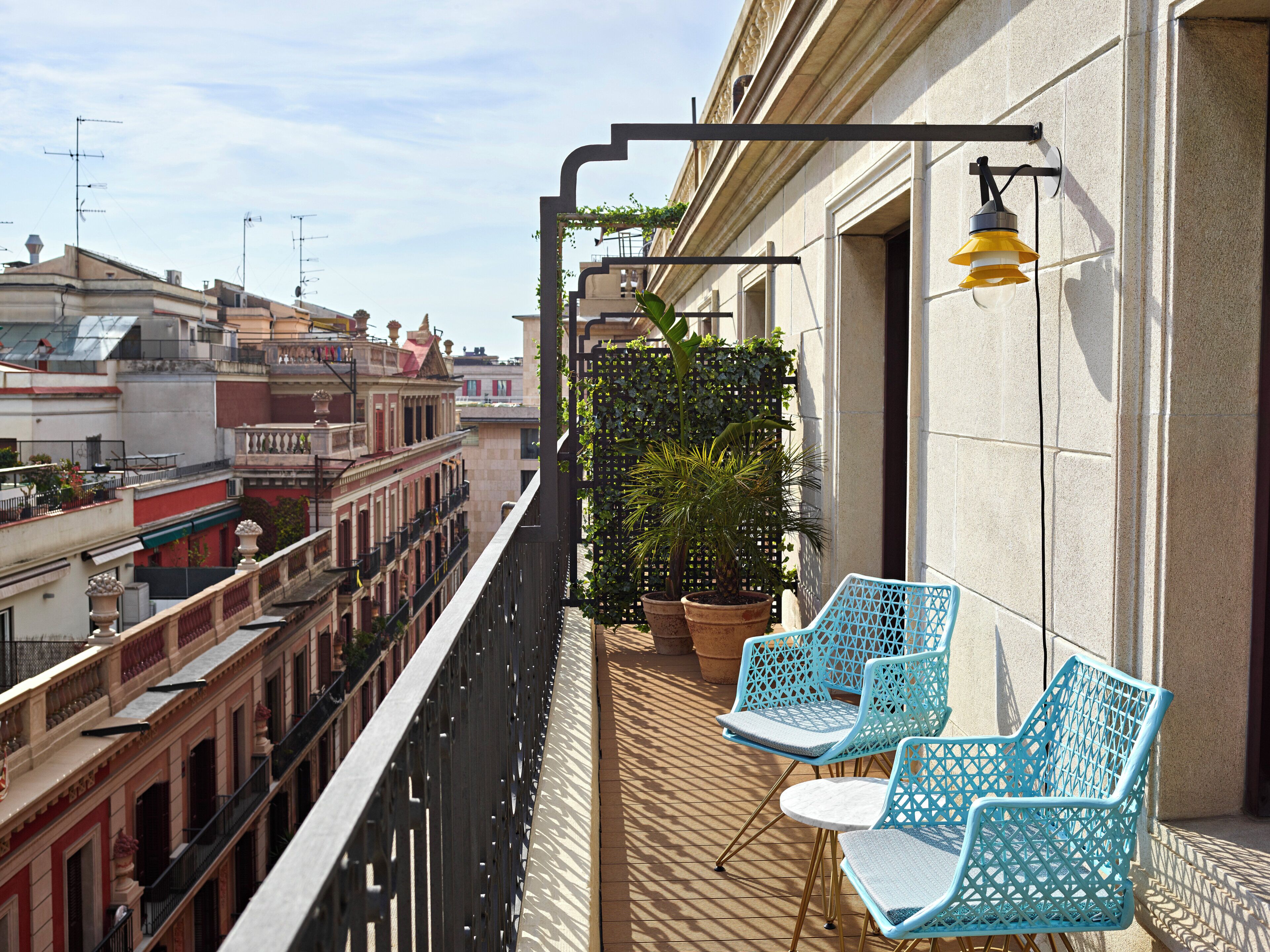 A balcony with two blue chairs, a potted plant, and a hanging light fixture.