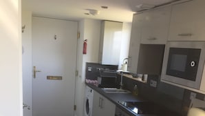 A compact kitchen with a washing machine, a microwave, and a sink. There are two red bar stools and a small countertop. - Cosy sea View Cottage Isle of Skye (Glendale)