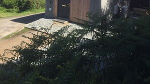 A small, single-story building with a red roof and a wooden door, surrounded by greenery and a clear sky. - Cosy sea View Cottage Isle of Skye (Glendale)