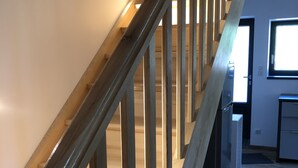 Een houten trap met een leuning, die leidt naar een kamer met een raam en een deur.