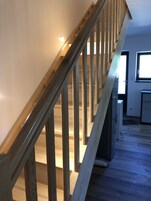 Una escalera de madera con barandilla, que lleva a una habitación con ventana y puerta.