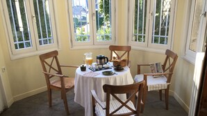Een eetgedeelte met een ronde tafel, vier houten stoelen, een witte tafelkleed en ontbijtartikelen.