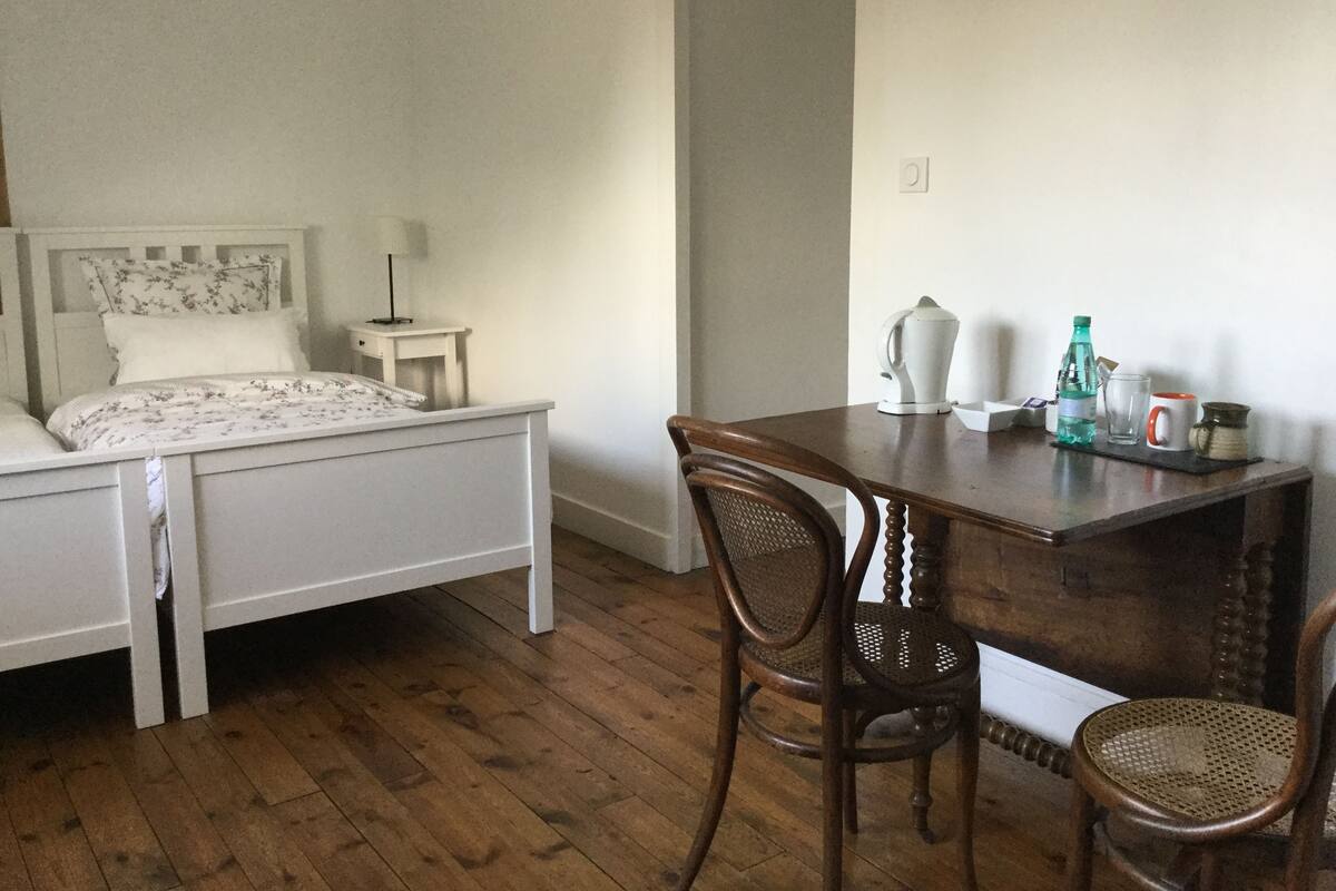 Een slaapkamer met een bed, nachtkastje, lamp en een bureau met stoelen.