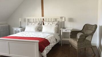 Une chambre à coucher avec un lit blanc, deux tables de chevet, une chaise en osier et un radiateur.