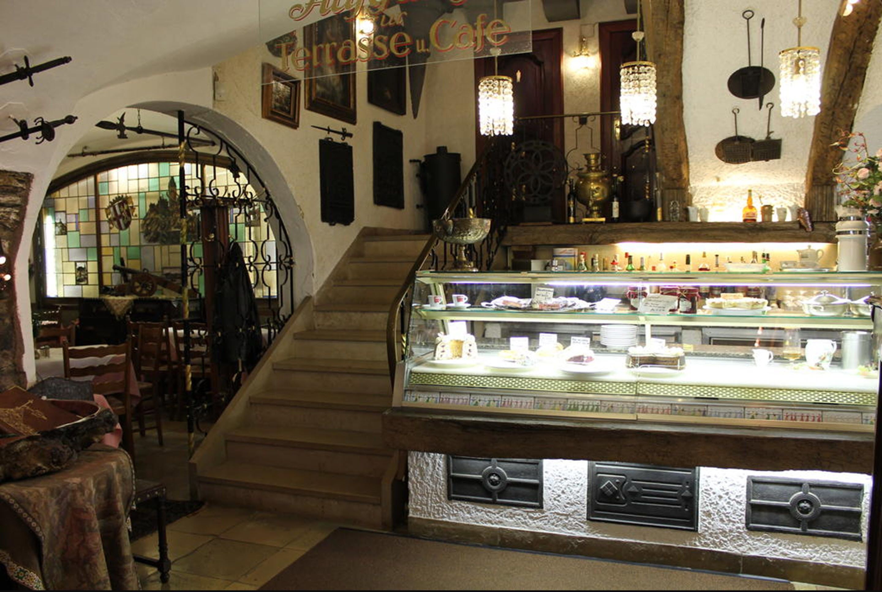 A café interior with a staircase, a glass display case with pastries, and vintage decor.