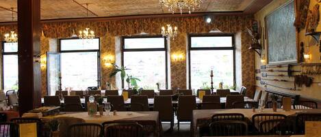 A restaurant with multiple tables and chairs, large windows, and a chandelier.