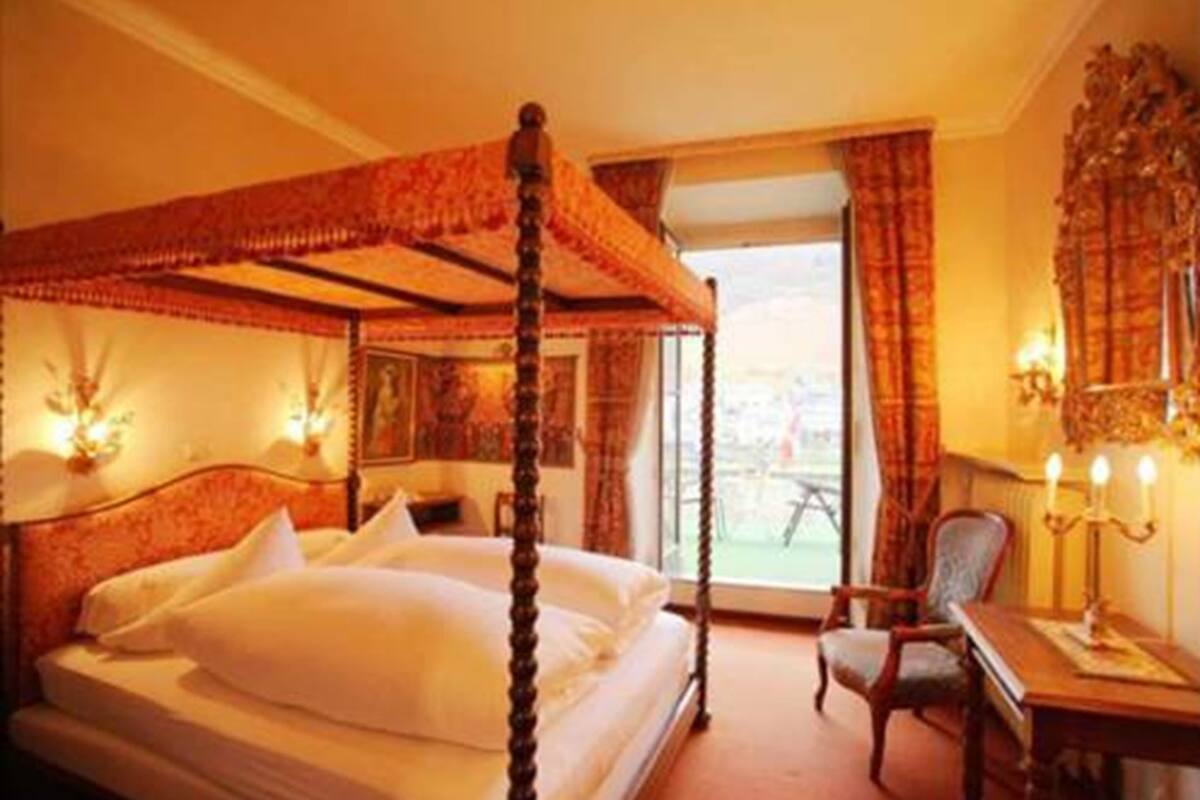 Una cama con dosel y mosquitera, un escritorio con lámpara y una silla en una habitación de hotel.