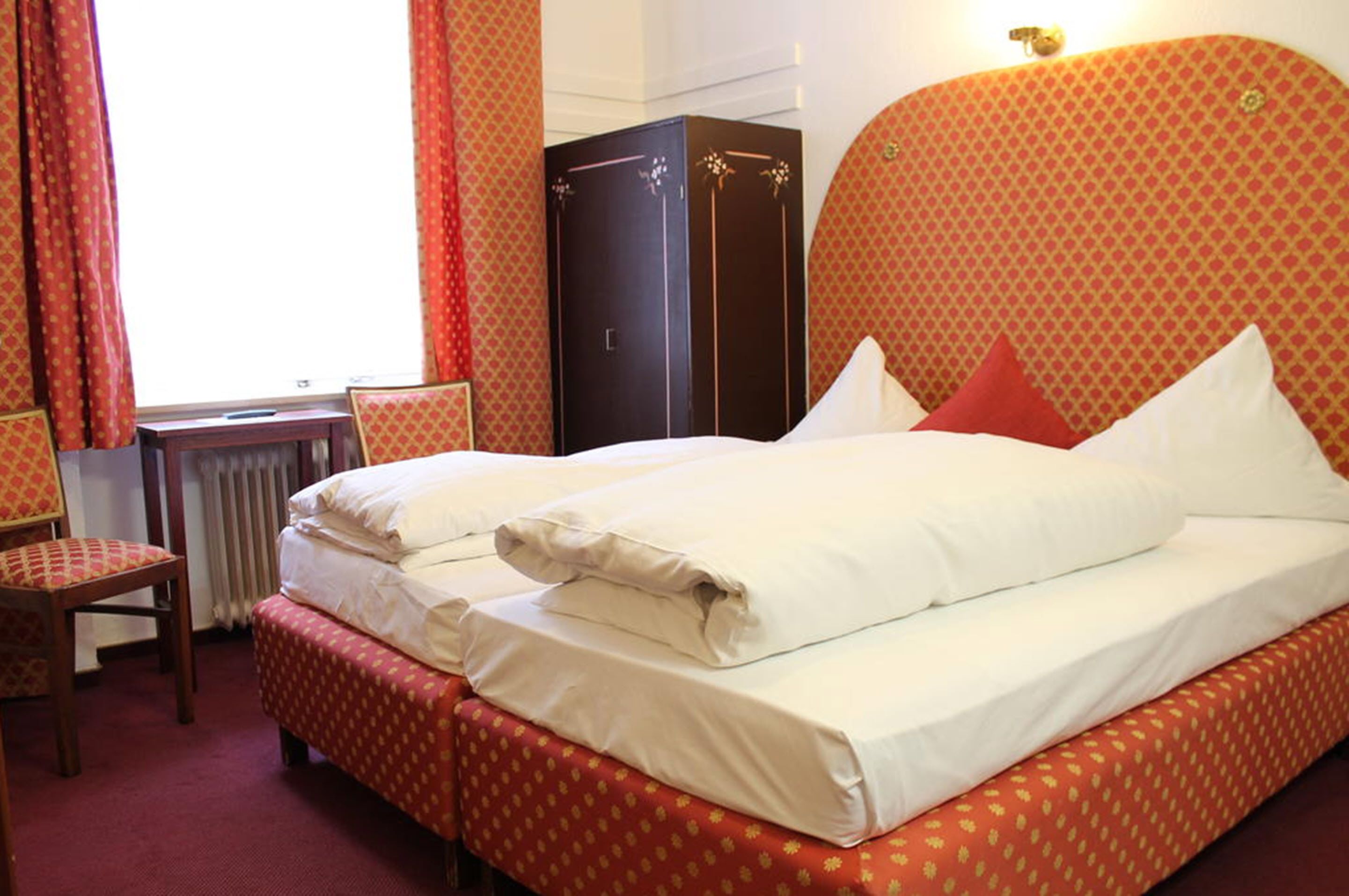Una habitación de hotel con cama, una silla, armario y radiador.