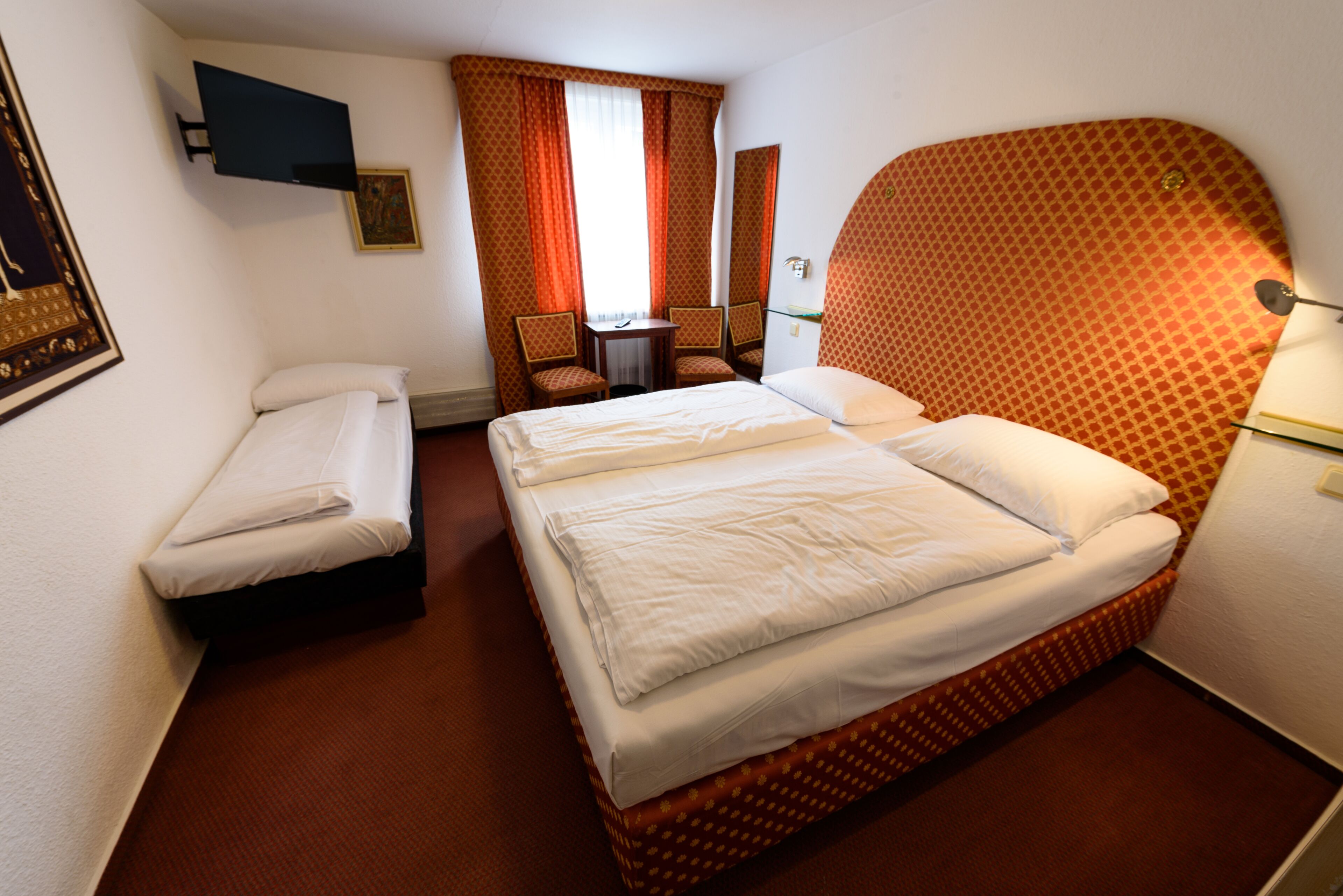 A hotel room with a large bed, a smaller bed, a desk with chairs, a TV, and a mirror.