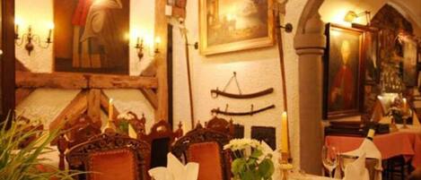 Un comedor con una mesa dispuesta para dos personas, que incluye un jarrón con flores, velas y un cuadro en la pared.