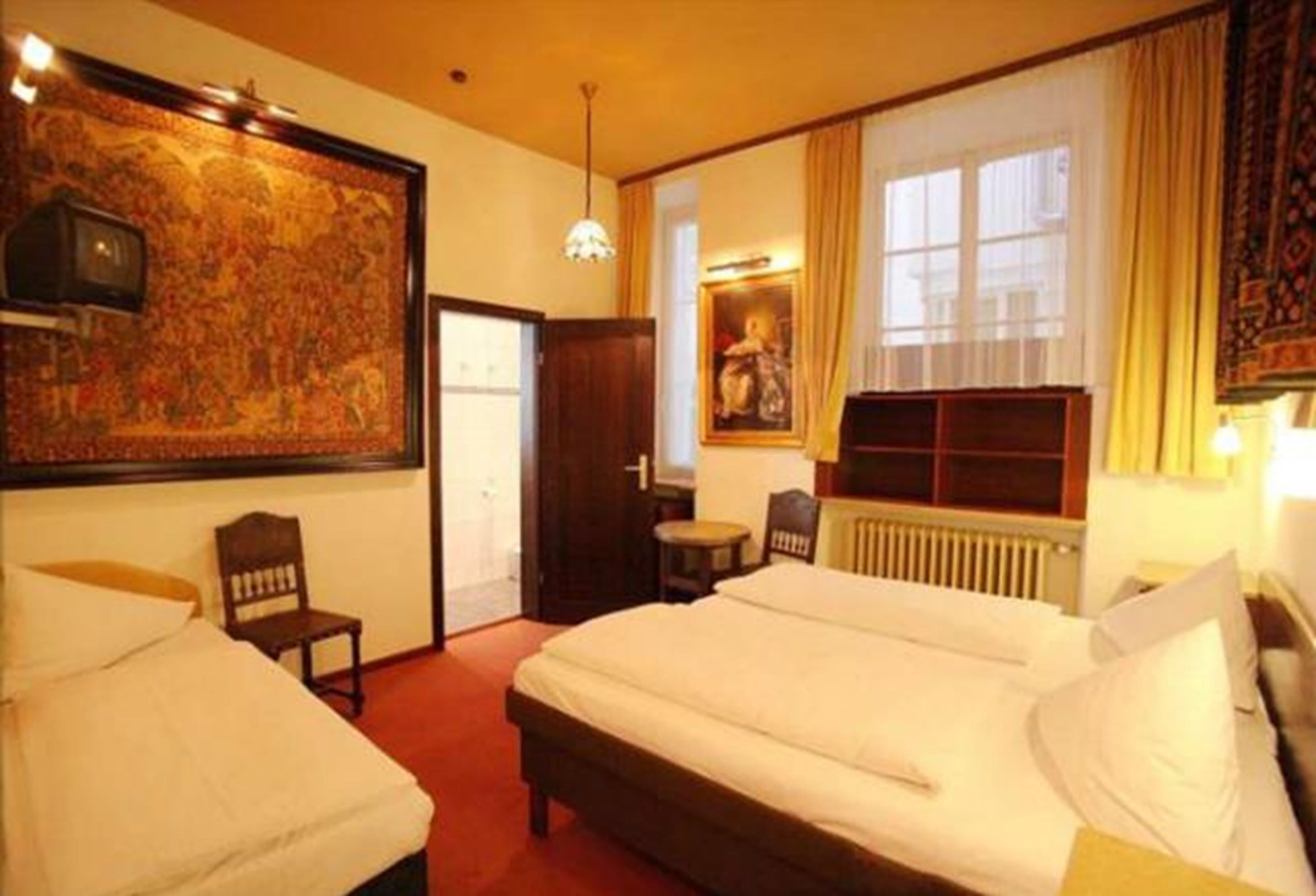 A hotel room with two beds, a large tapestry, a radiator, and a window with curtains.