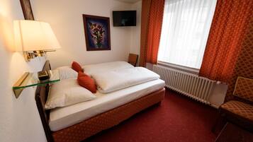 A hotel room with a bed, a TV, a painting, a chair, and a window with curtains.