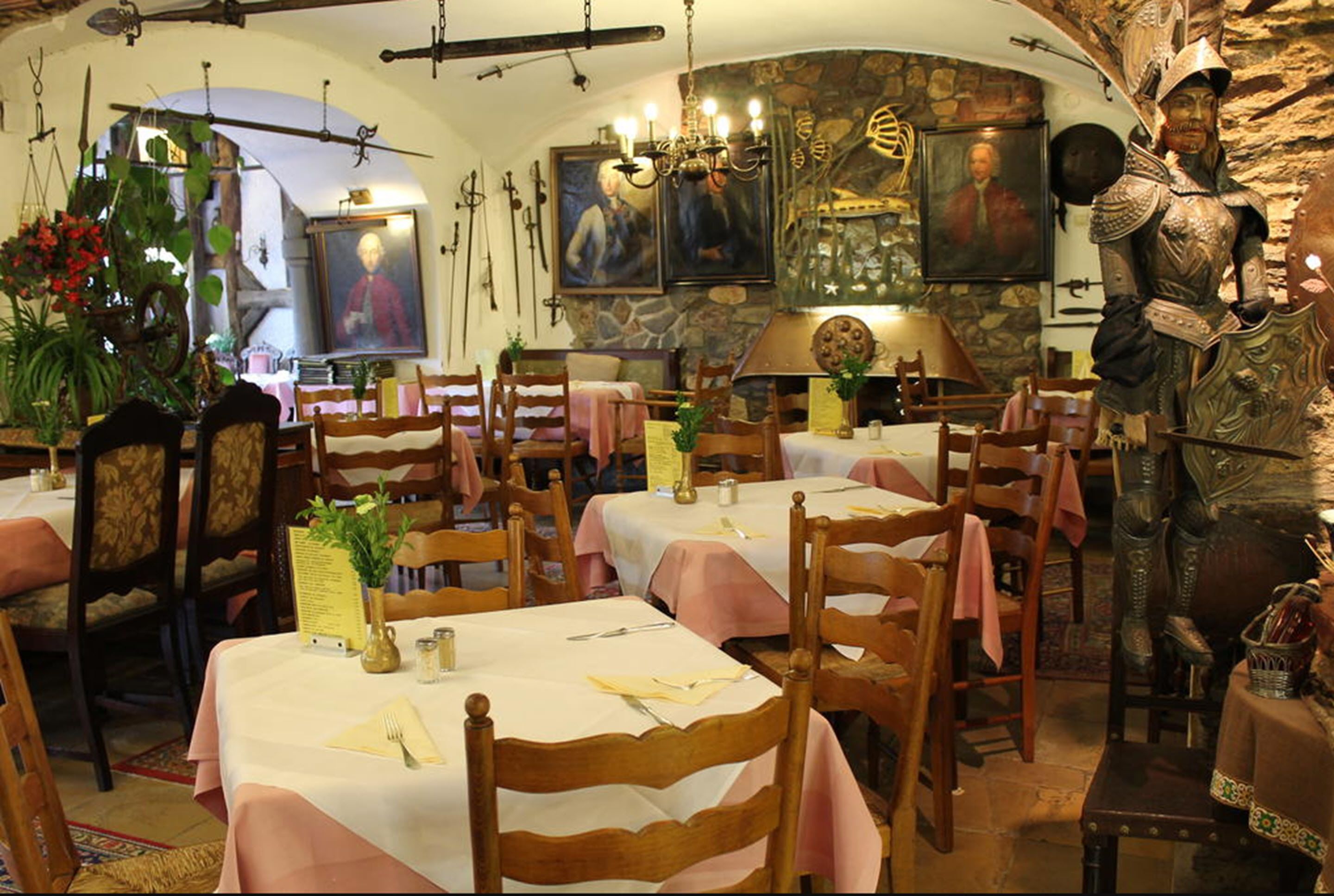 Un restaurante con mesas y sillas de madera, paredes de piedra y una estatua de un caballero medieval.