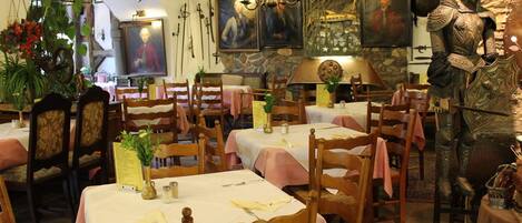 A restaurant with wooden tables and chairs, stone walls, and a medieval knight statue.